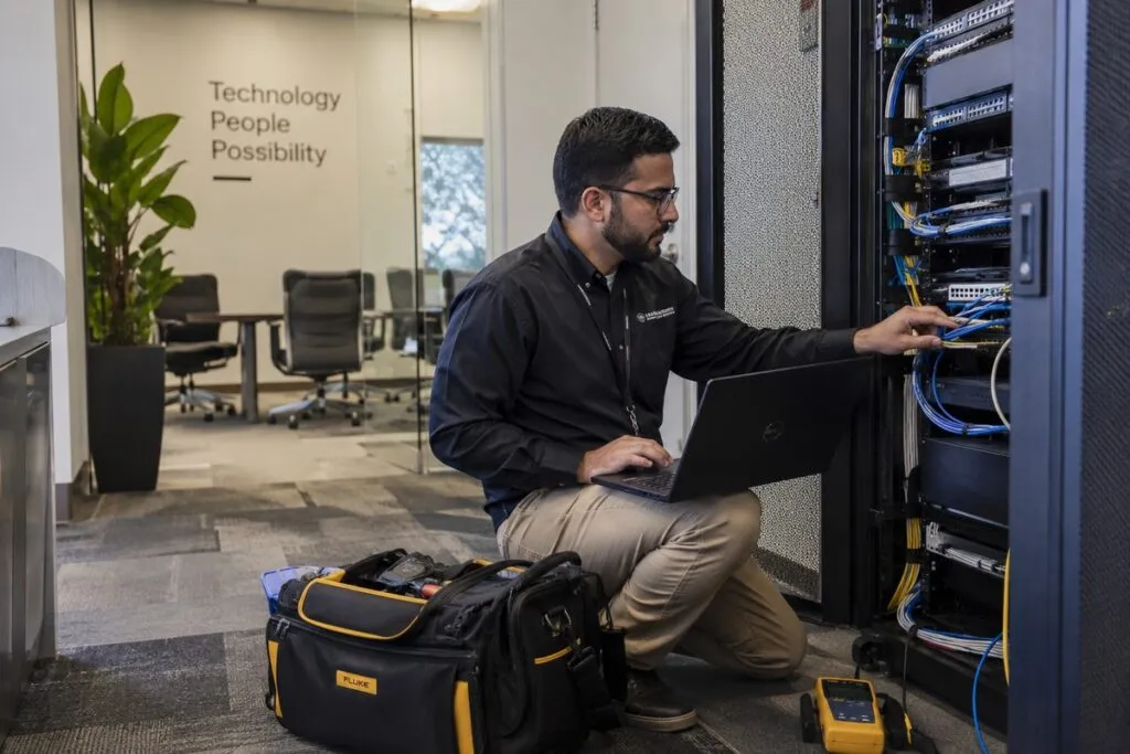 Qualified IT field technician servicing business network equipment with professional testing tools and laptop.